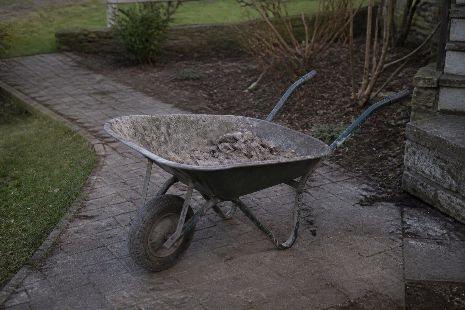 A wheelbarrow half loaded and left standing on a path