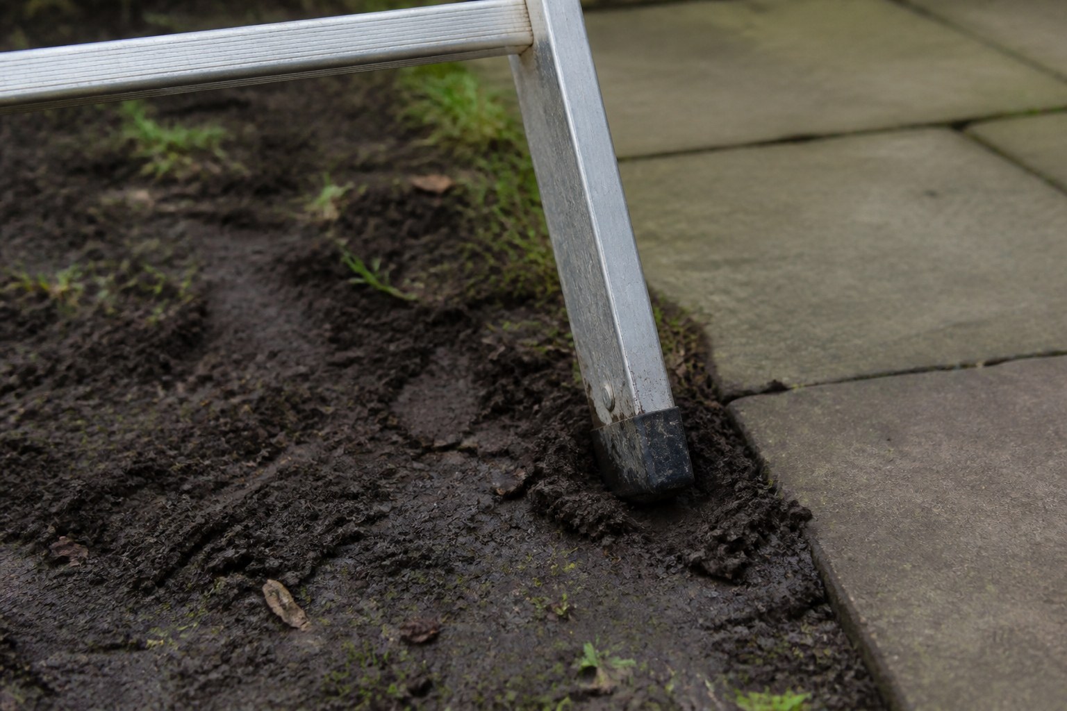 A ladder footed on soft ground immediately beside firm paving