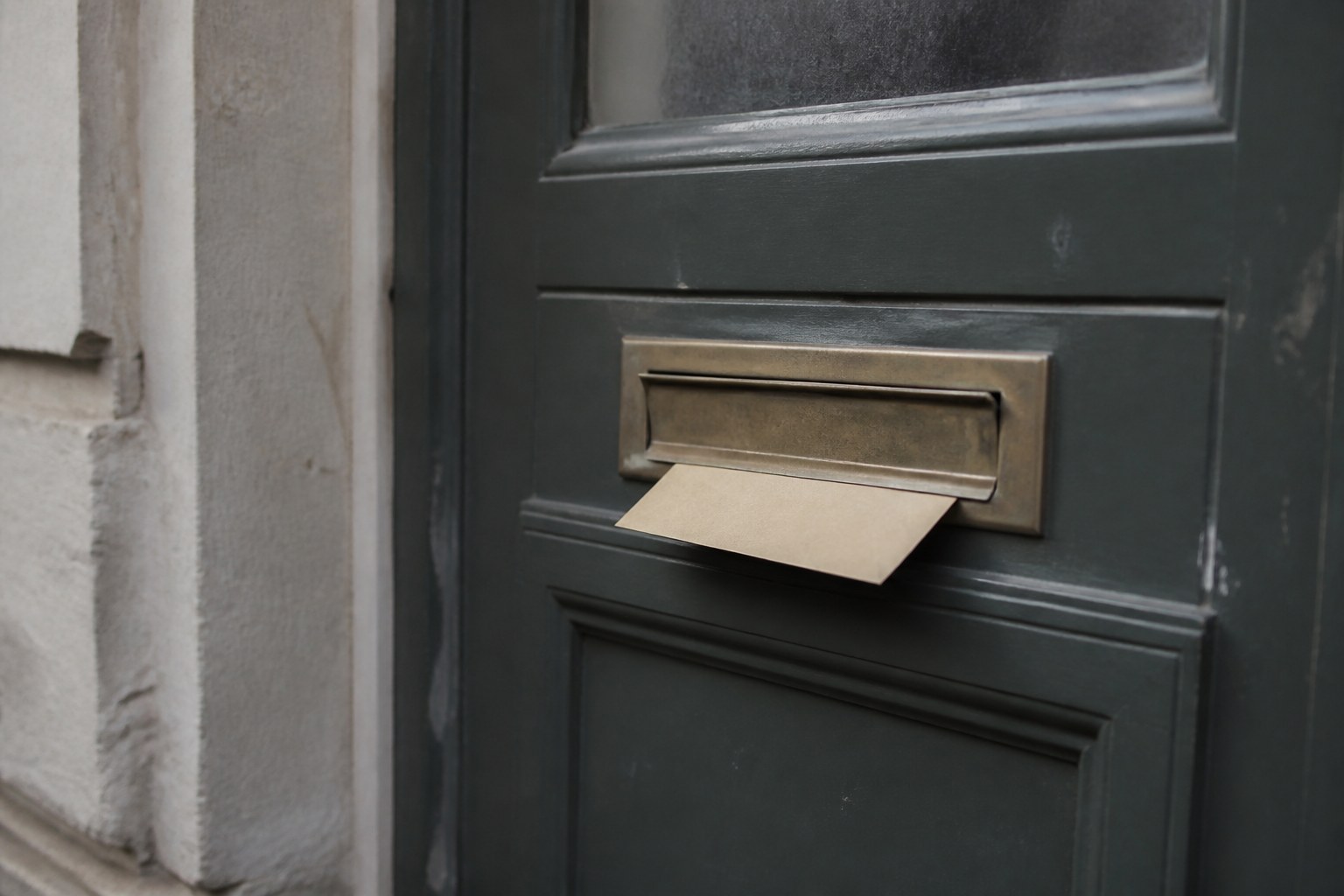 A brass letterbox with an envelope caught half through the slot