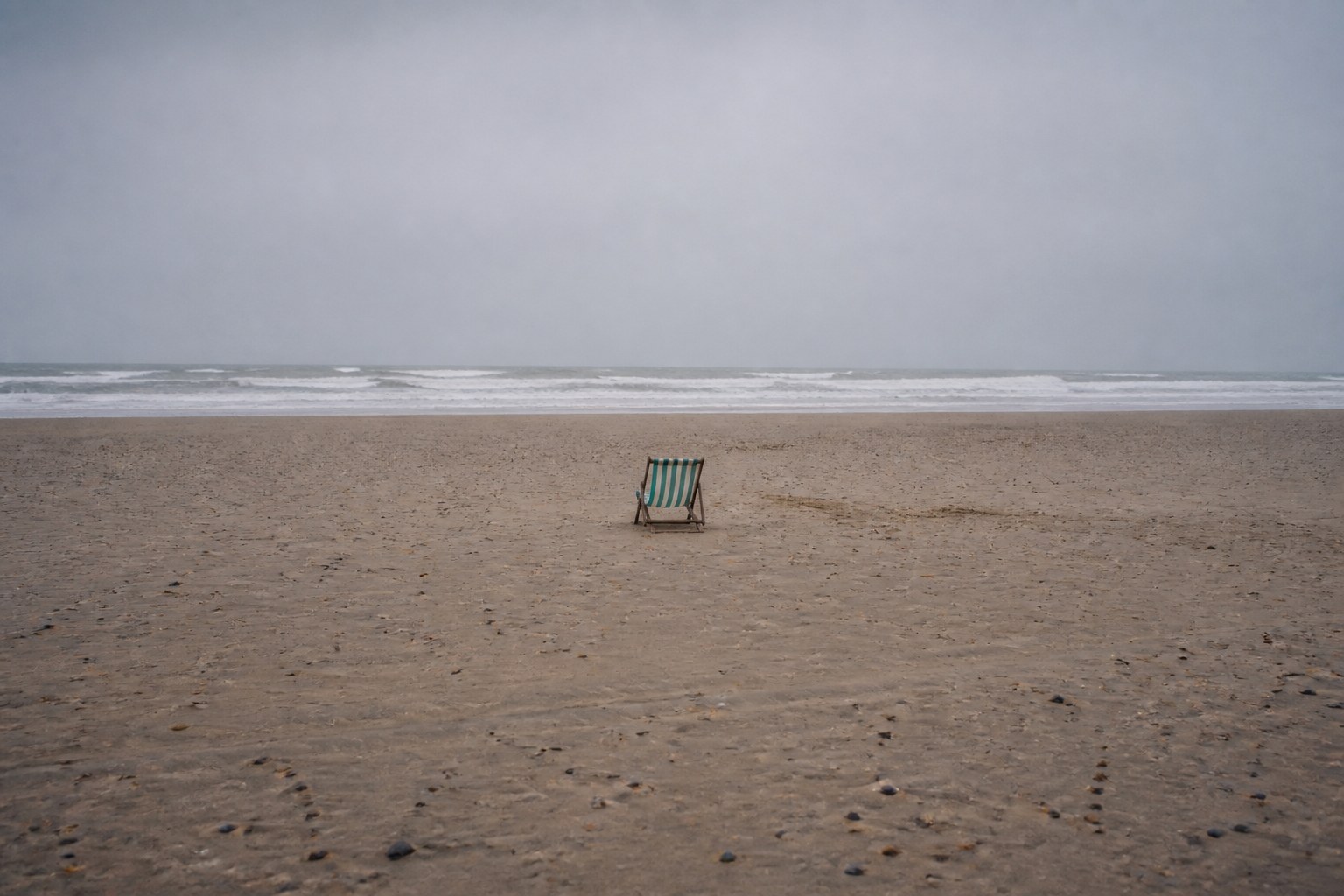A single deckchair set far out on a wide empty beach