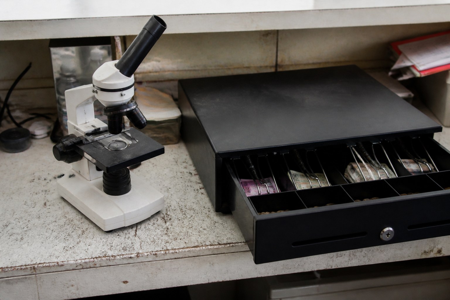 A microscope and an open cash drawer on the same workbench