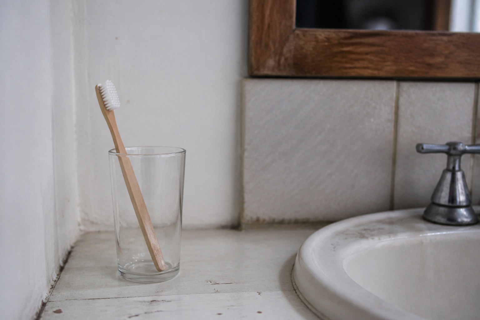 A single toothbrush in a glass beside a bathroom sink with room for another