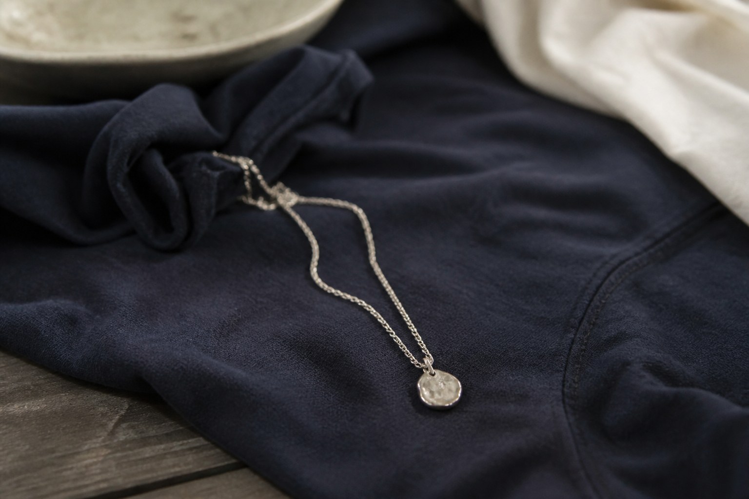 A small silver pendant on a fine chain lying on dark cloth