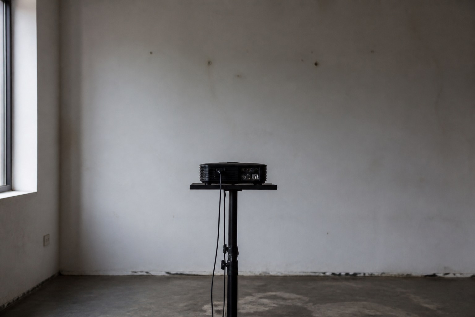 A projector switched off facing a blank wall in an empty room