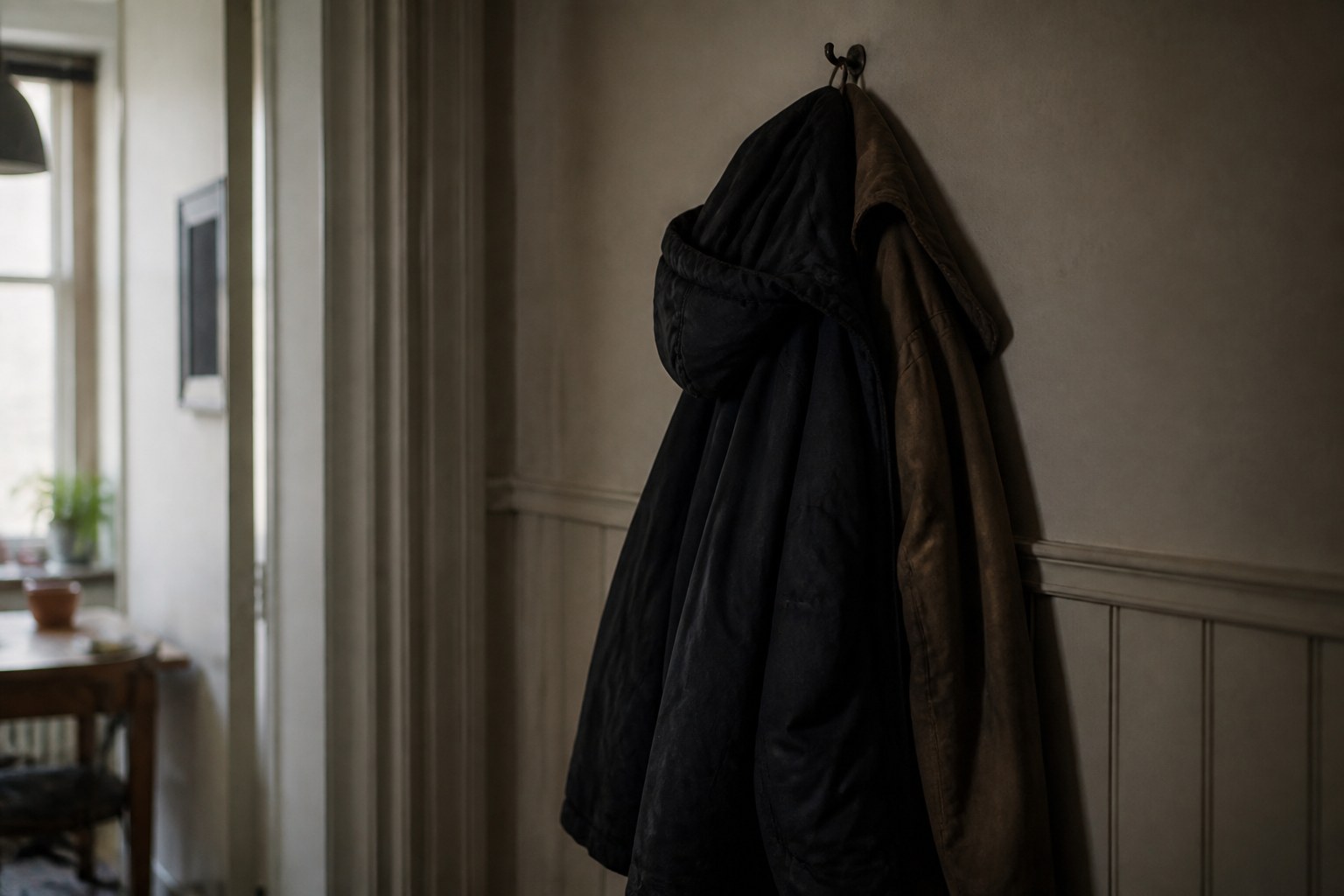 Two winter coats hung on the same peg, one over the other, in a narrow hallway