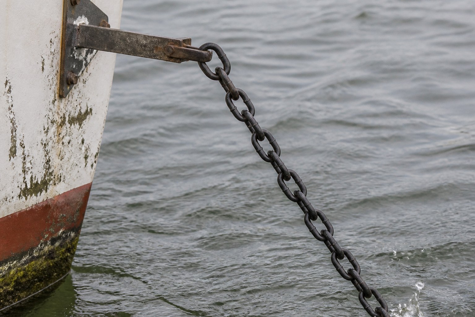 An anchor chain running taut from a boat's bow into moving water