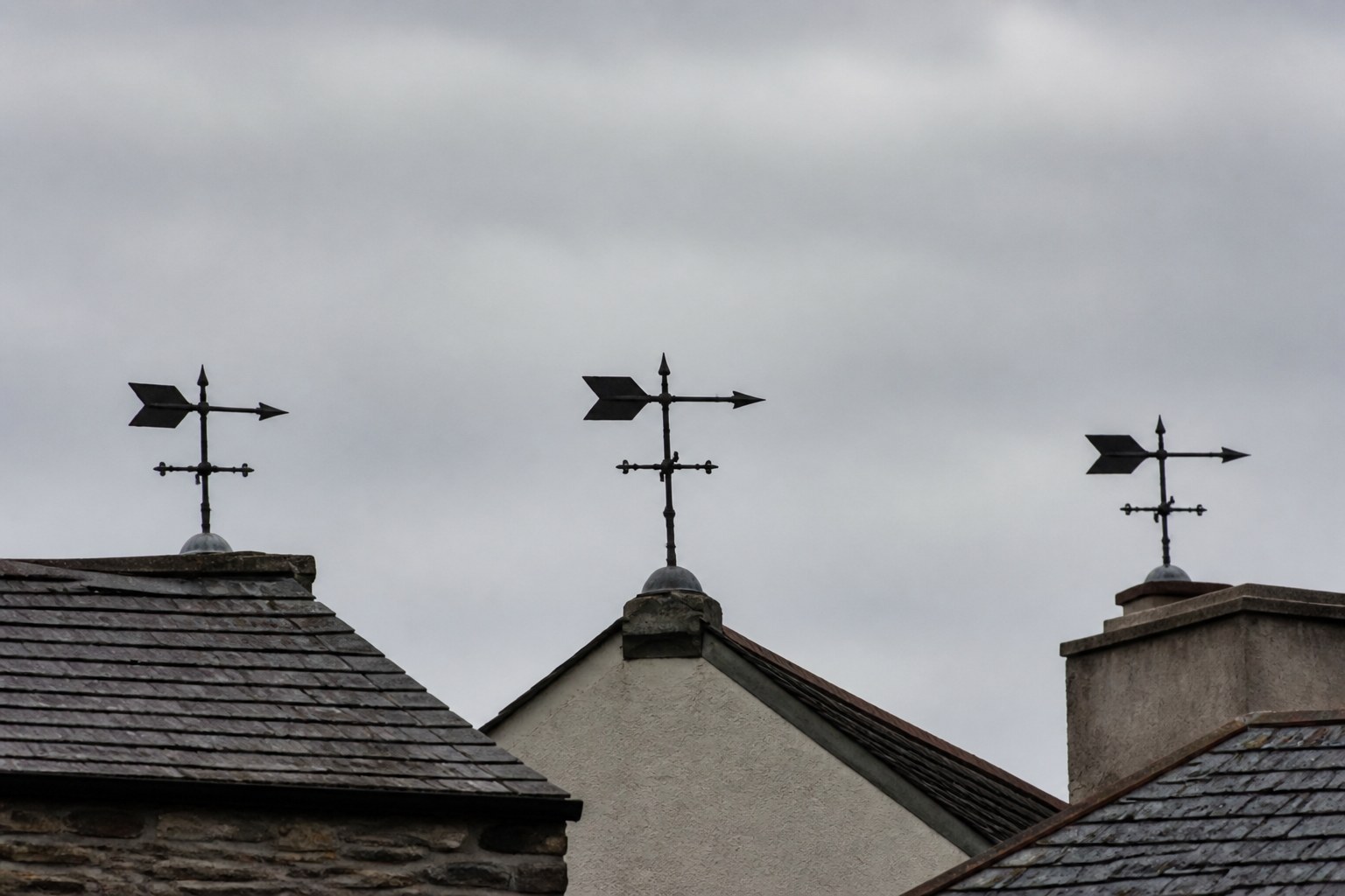 Three weather vanes on adjacent rooftops all pointing the same way