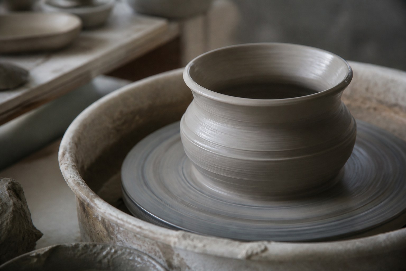 A wet thrown pot still turning on a potter's wheel, hands out of frame