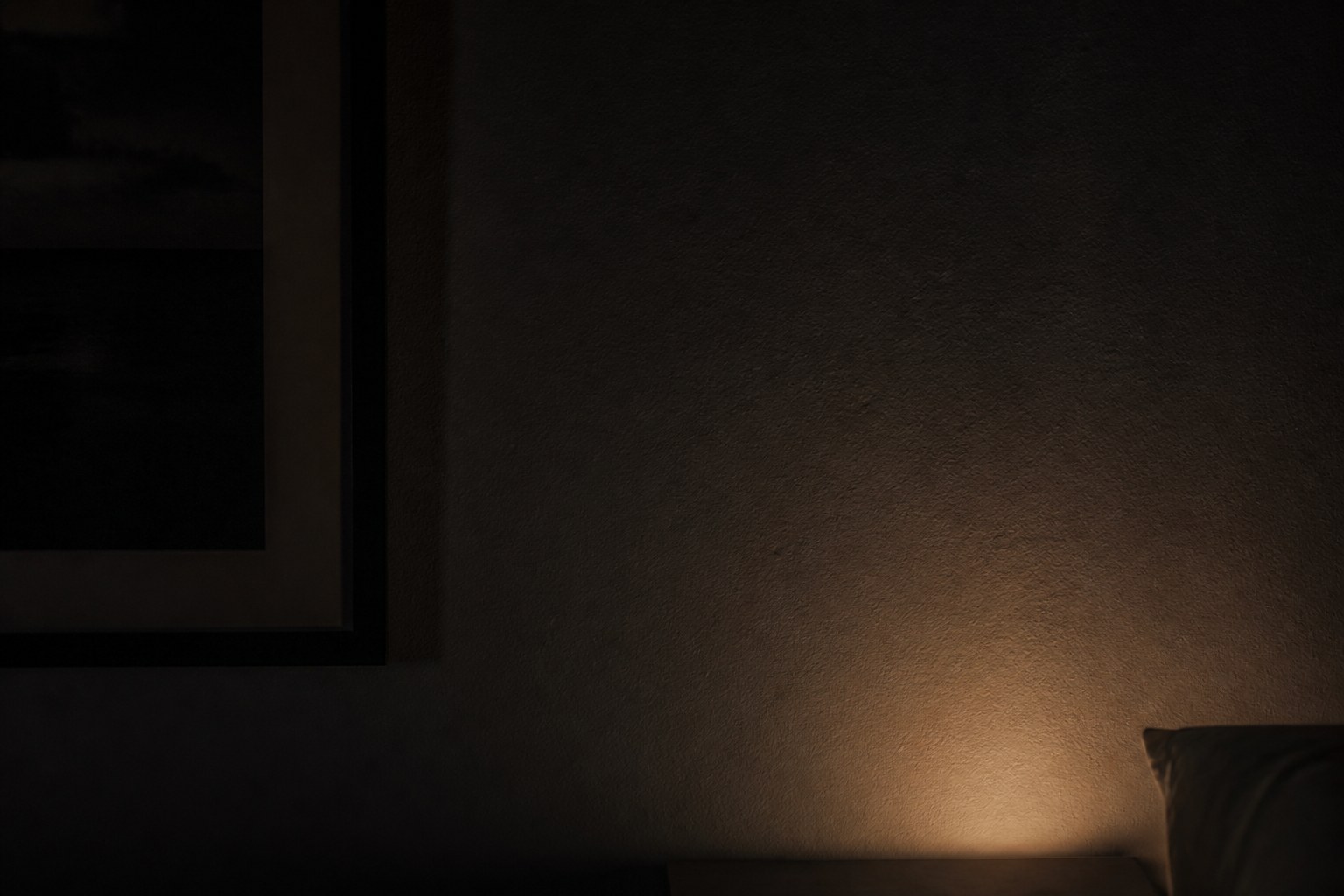 The soft glow of a bedside alarm reflected on a dark bedroom wall, the display itself out of frame