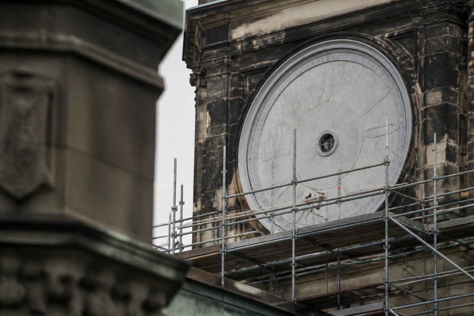 A large public clock face under repair with its hands removed, scaffolding standing against the tower
