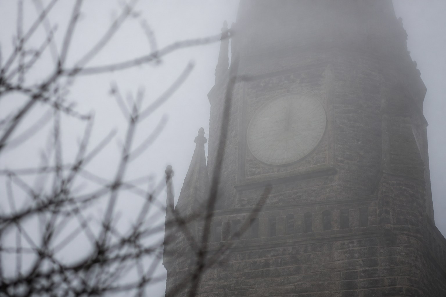 A church tower clock in thick fog, the face pale and indistinct behind the mist