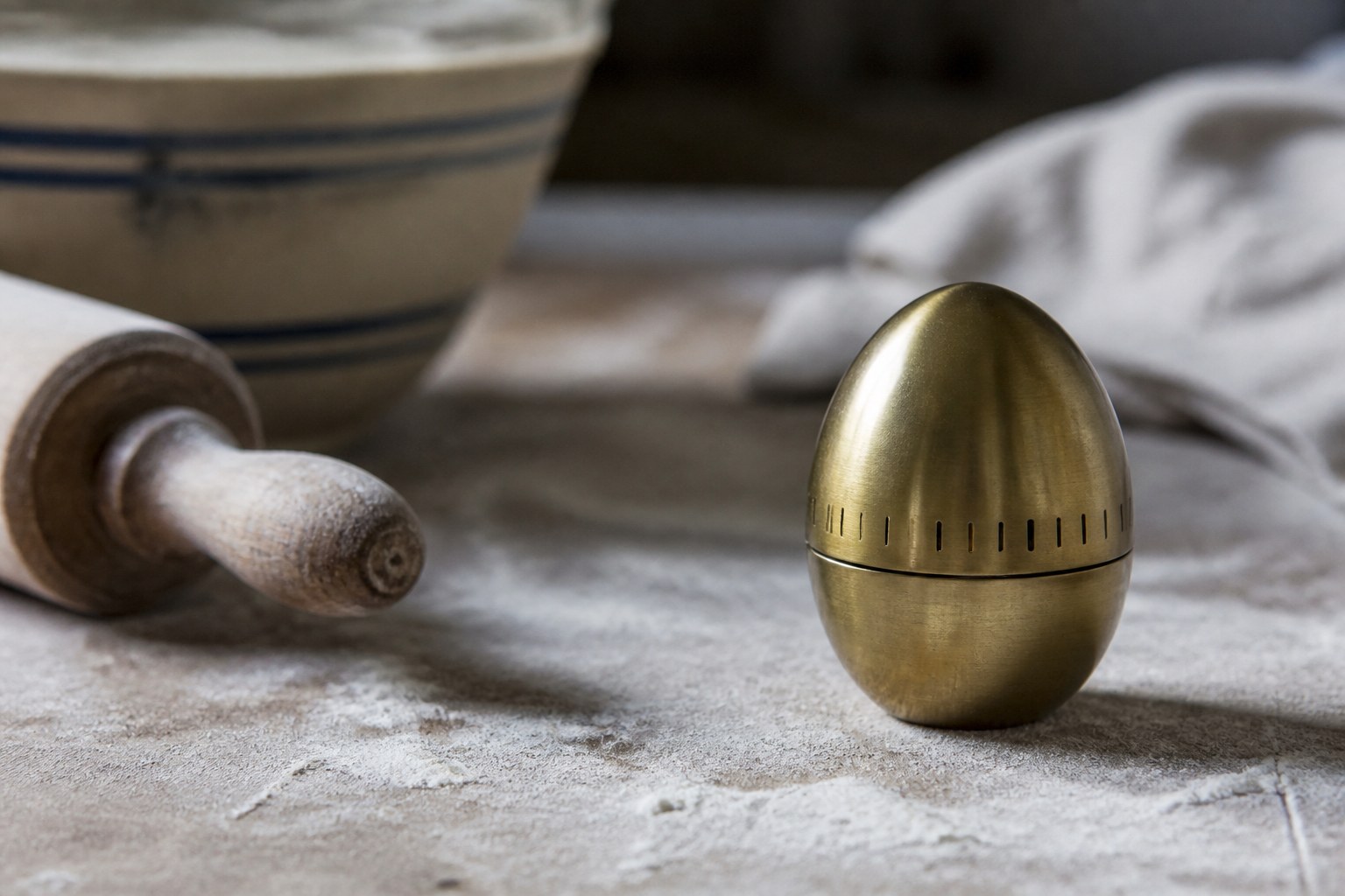 A brass kitchen egg timer standing on a floured worktop