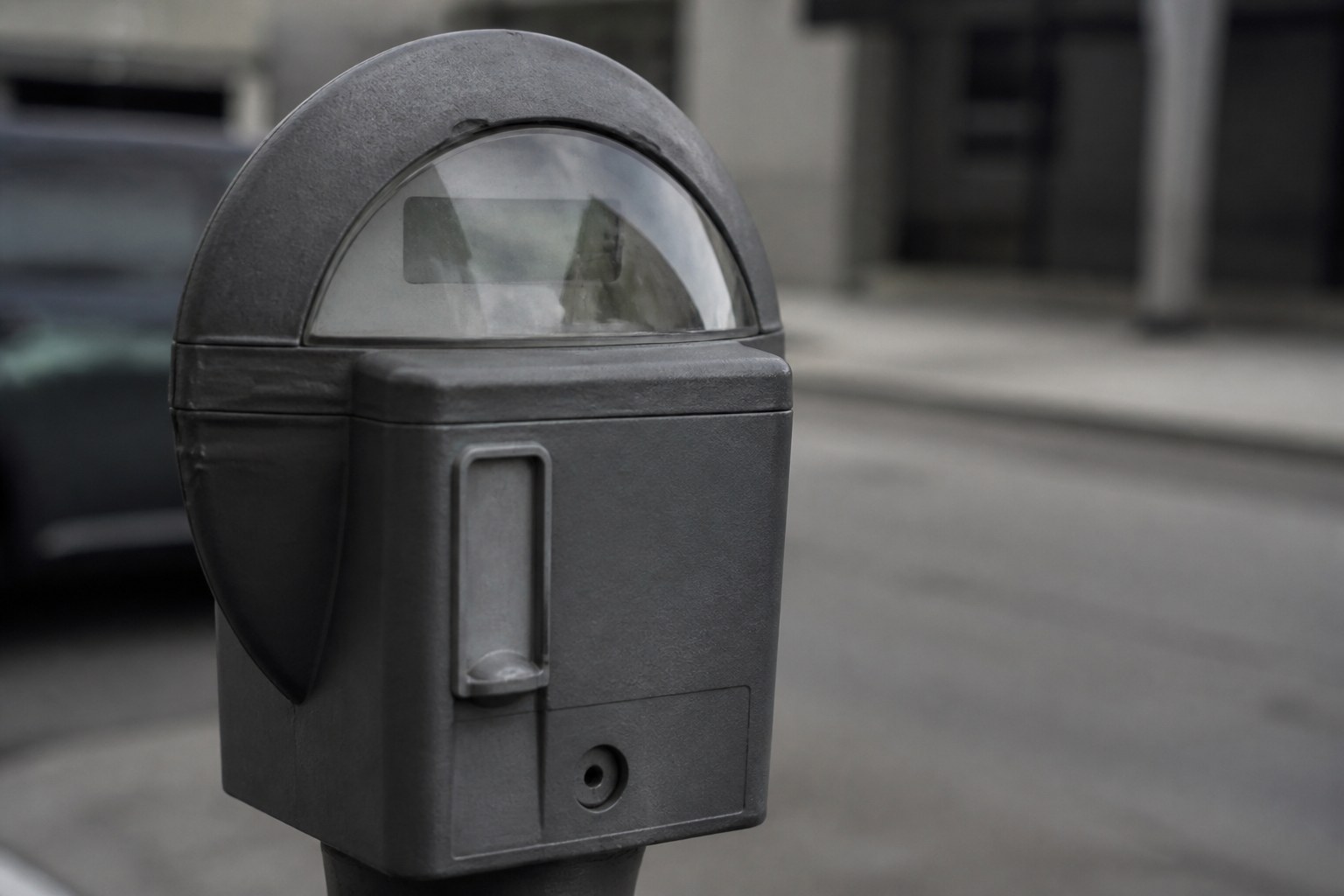A pavement parking meter in flat grey light, its window catching a reflection