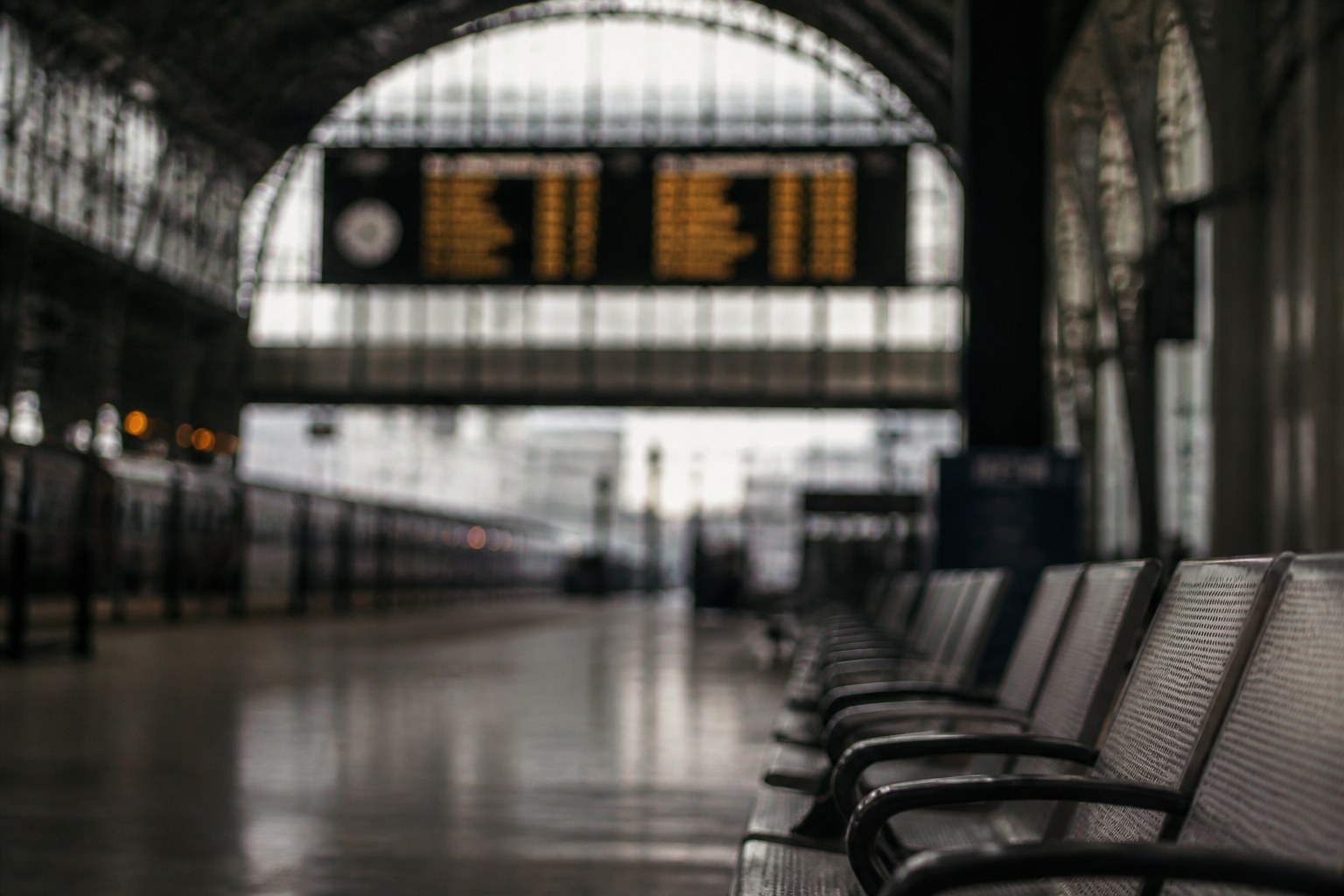 A blurred departure board seen from far down a station concourse, the figures unreadable