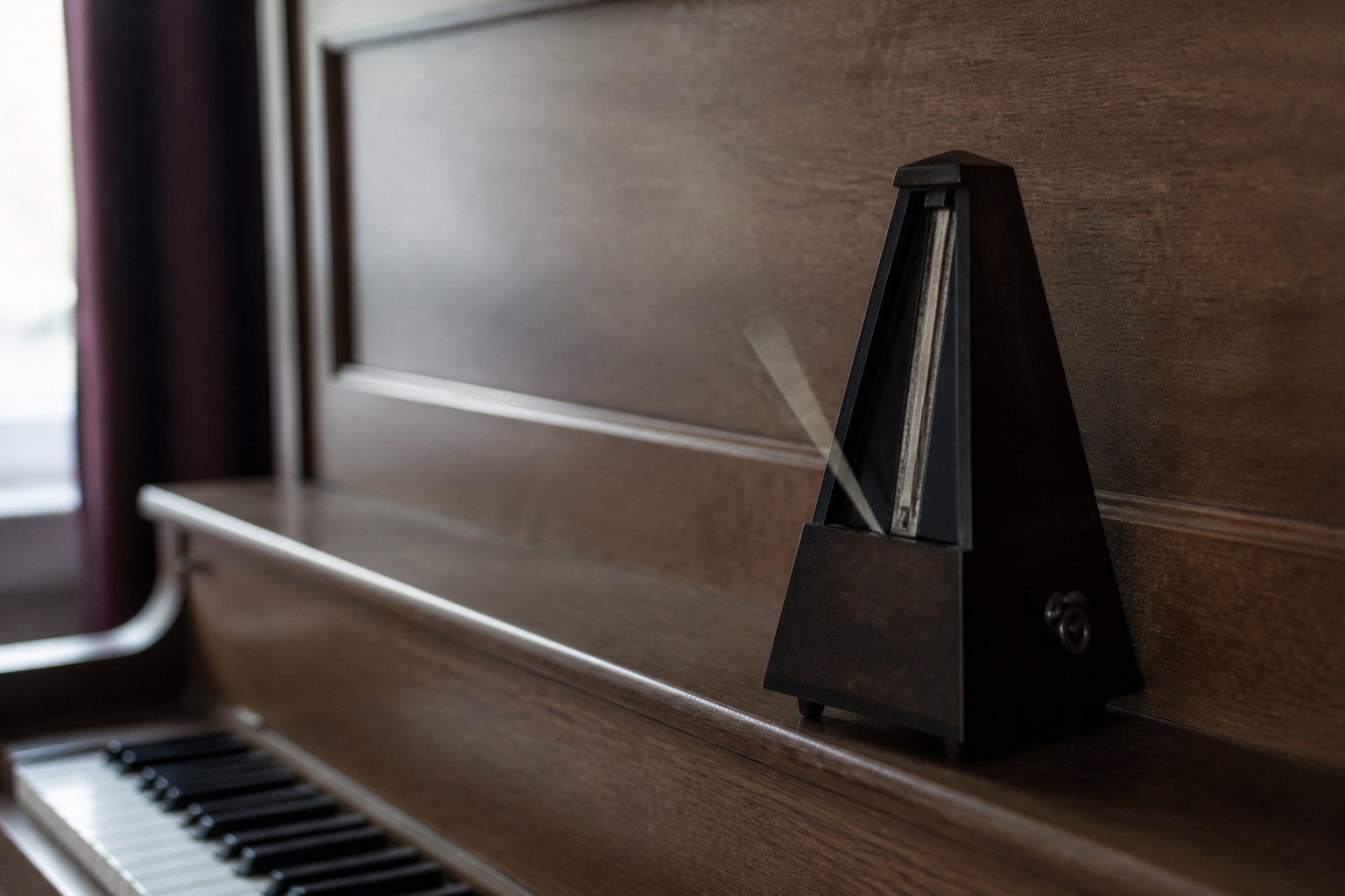 A metronome standing on an upright piano with its pendulum arm caught mid swing