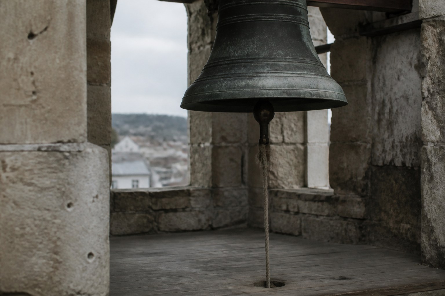 A tower bell hanging in a stone belfry with its rope disappearing through the floor