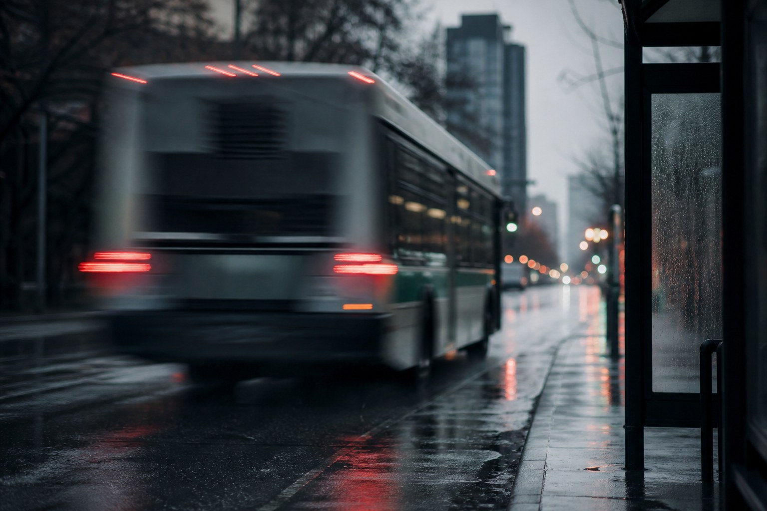 A commuter bus pulling away from a stop in the rain, its rear lights smeared