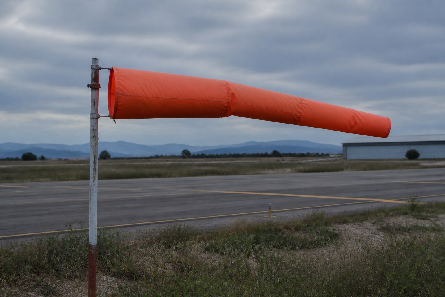 An orange windsock stretched horizontal on its pole at an airfield