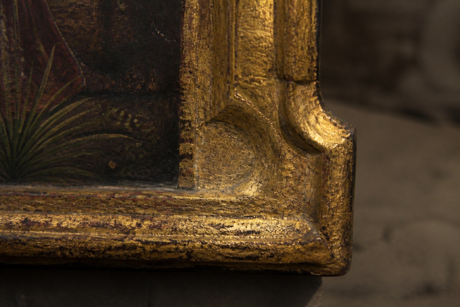 The gilded corner of an old icon panel under raking light, worn gold leaf and cracked paint visible along the edge