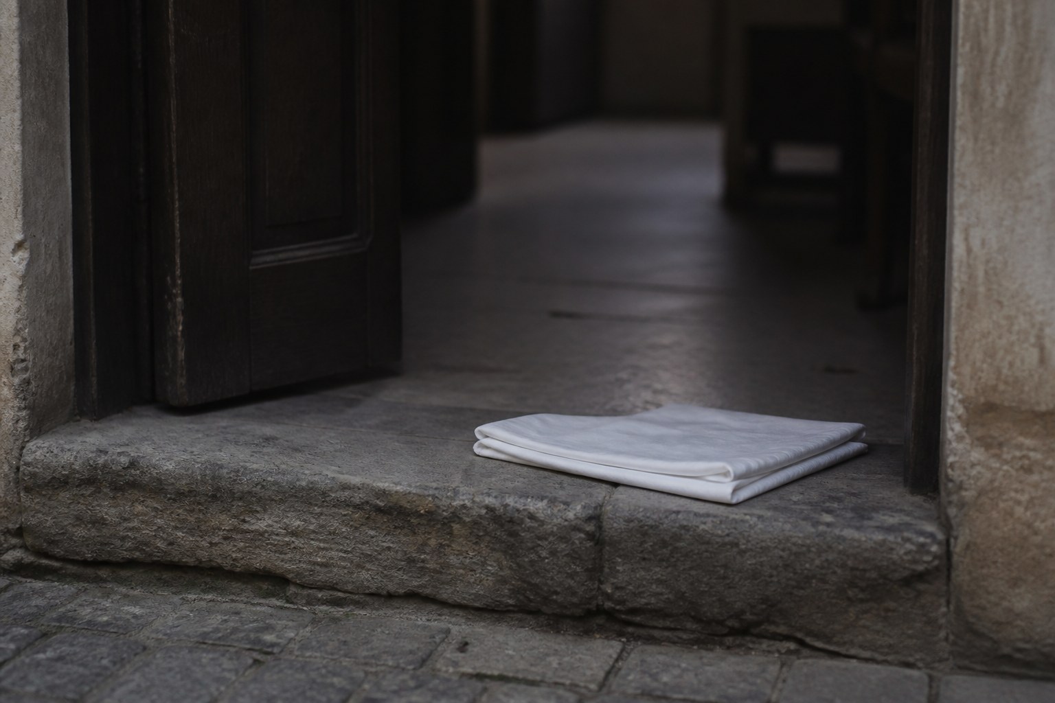A worn stone doorway threshold with a plain white cloth folded on the sill and a dark open door beyond