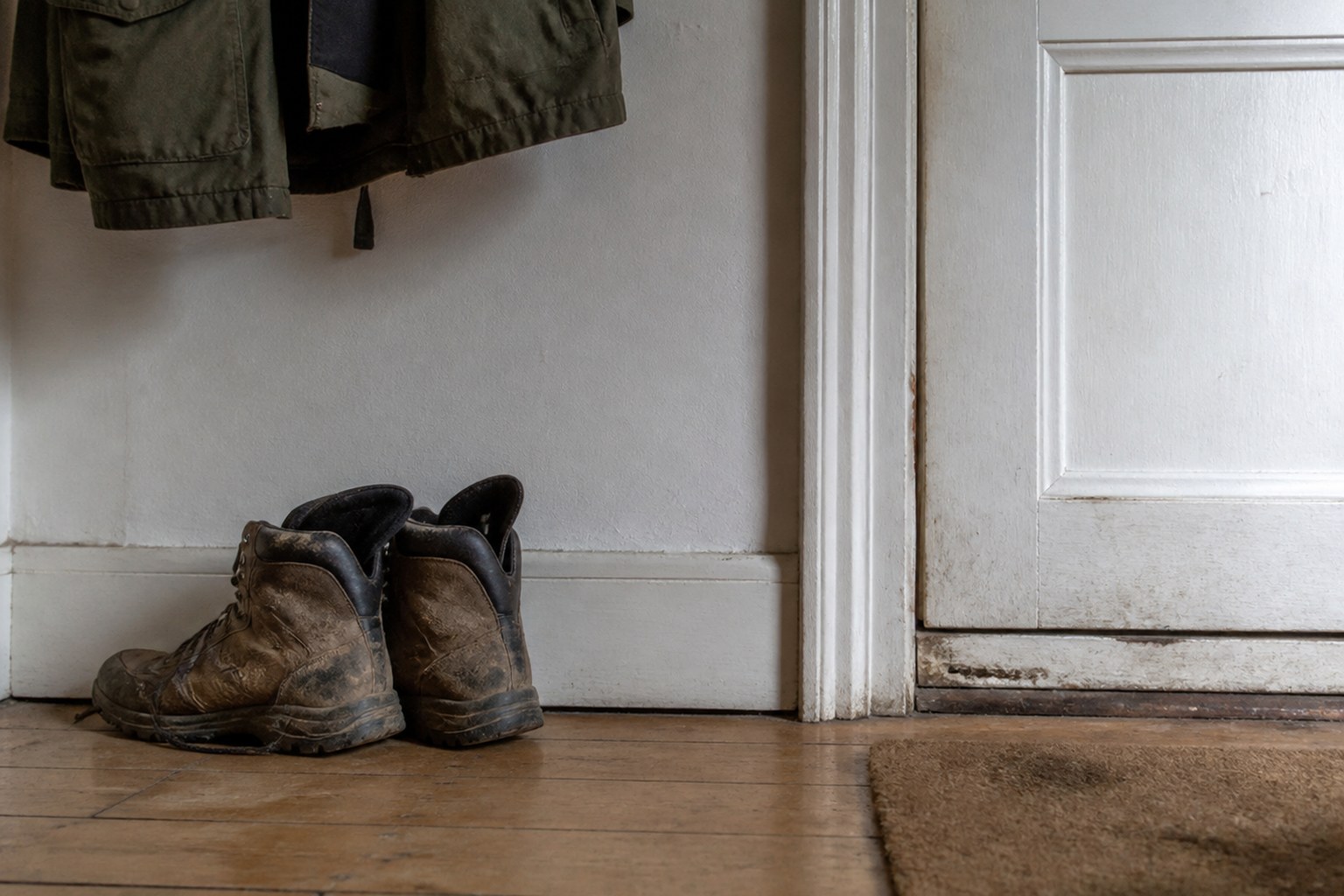 A pair of worn walking boots by a front door with a coat hanging above them