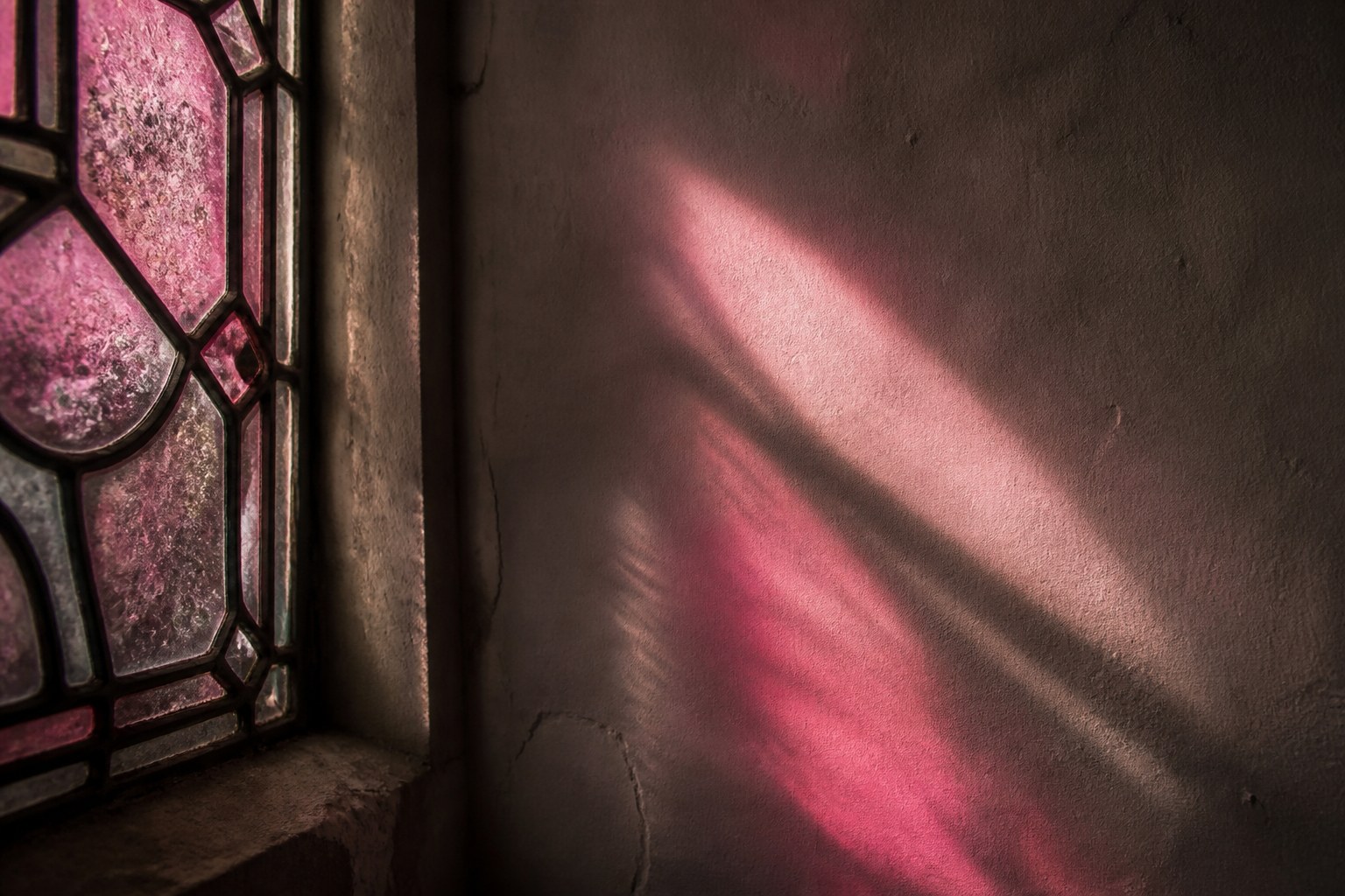 Rose coloured light thrown through a fragment of old stained glass onto a plain plaster wall