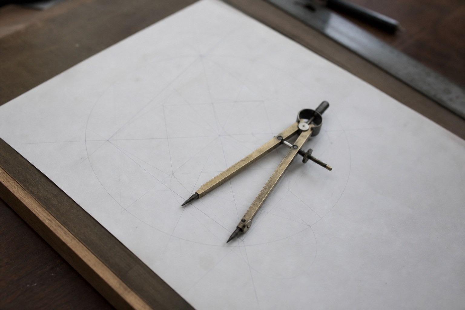 A pair of brass dividers resting on a geometric drawing on a drawing board
