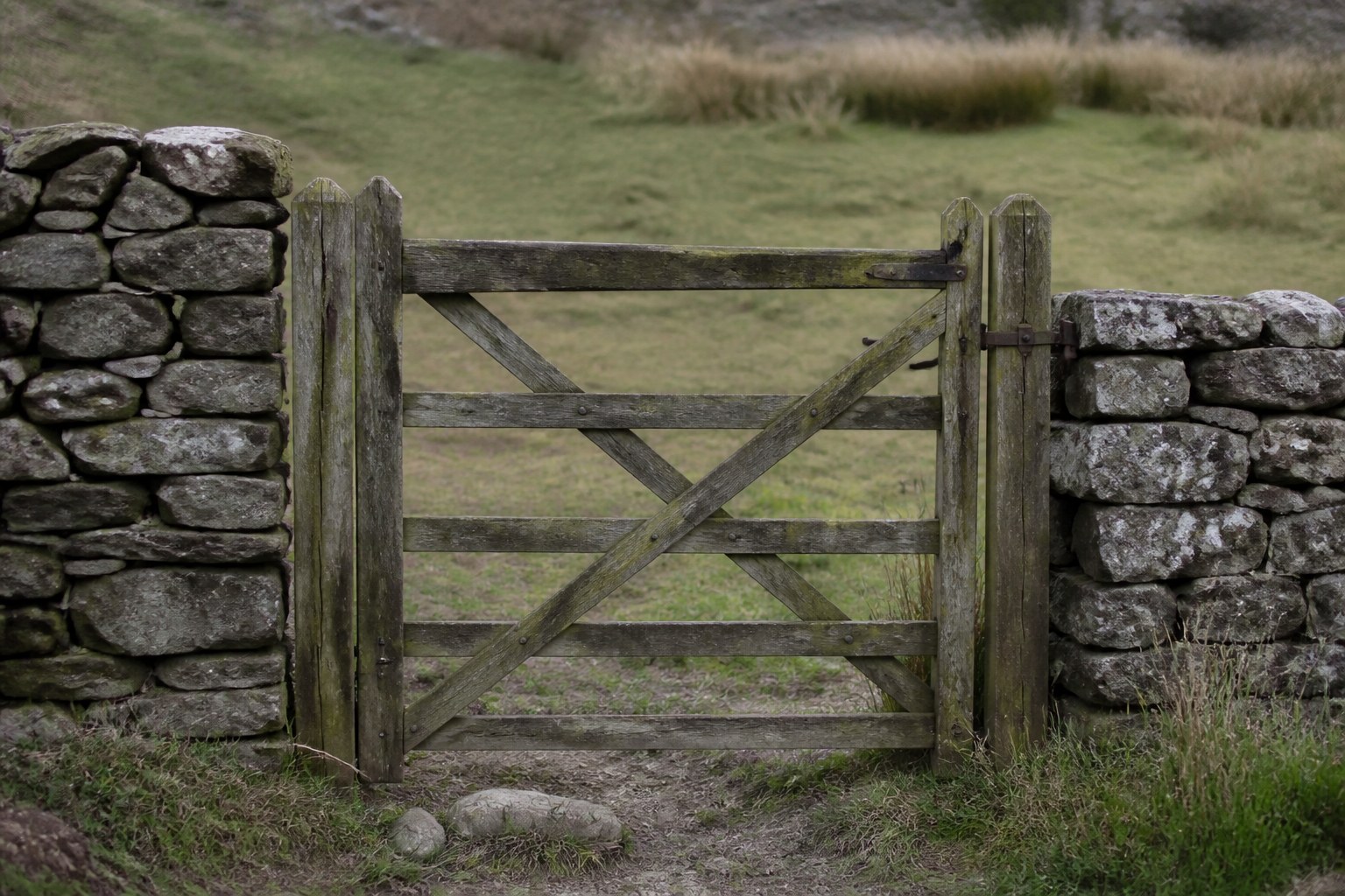 A closed wooden gate set into a low dry stone wall at a field boundary