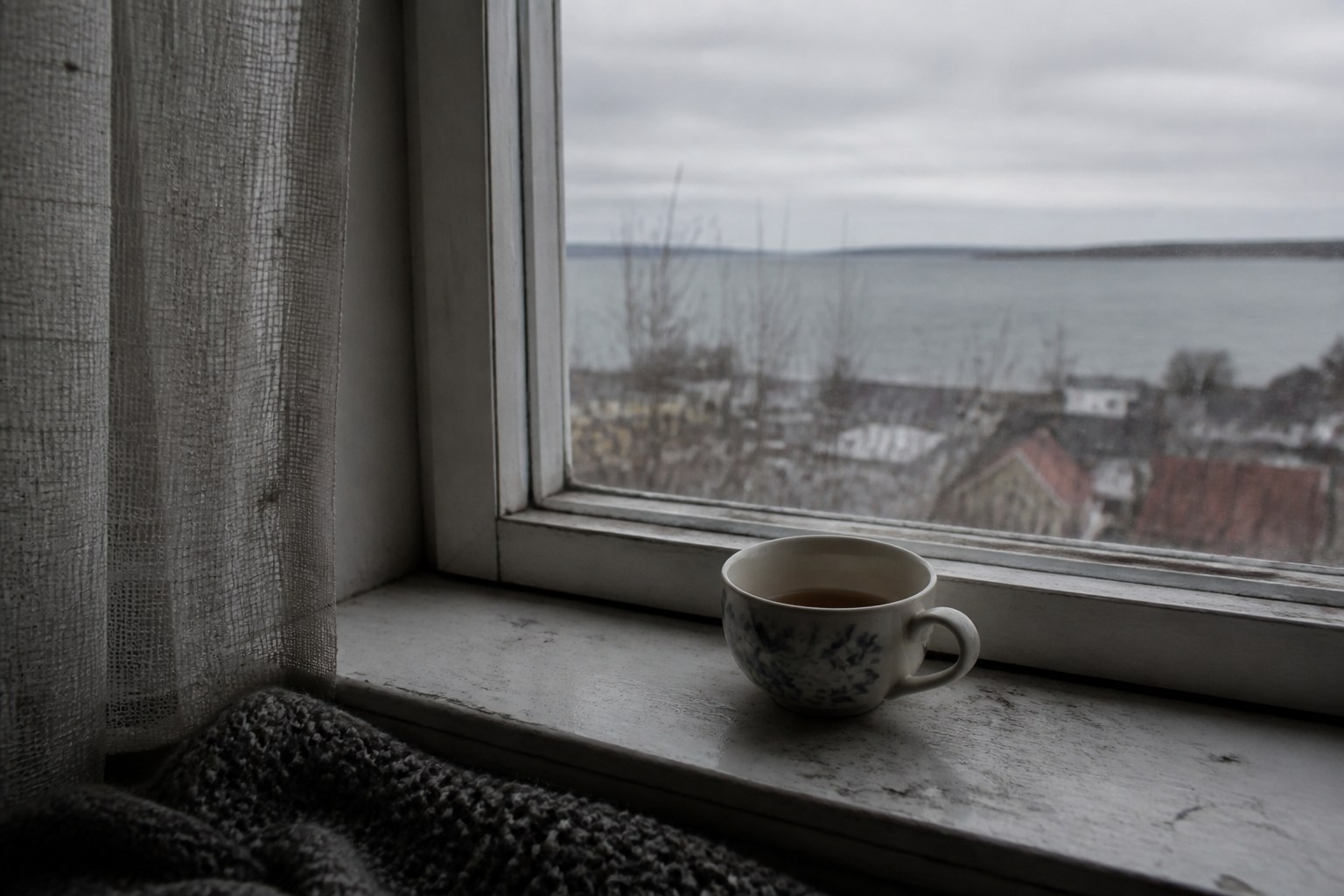 A windowsill under a flat overcast sky with a cold half finished cup of tea left standing on it