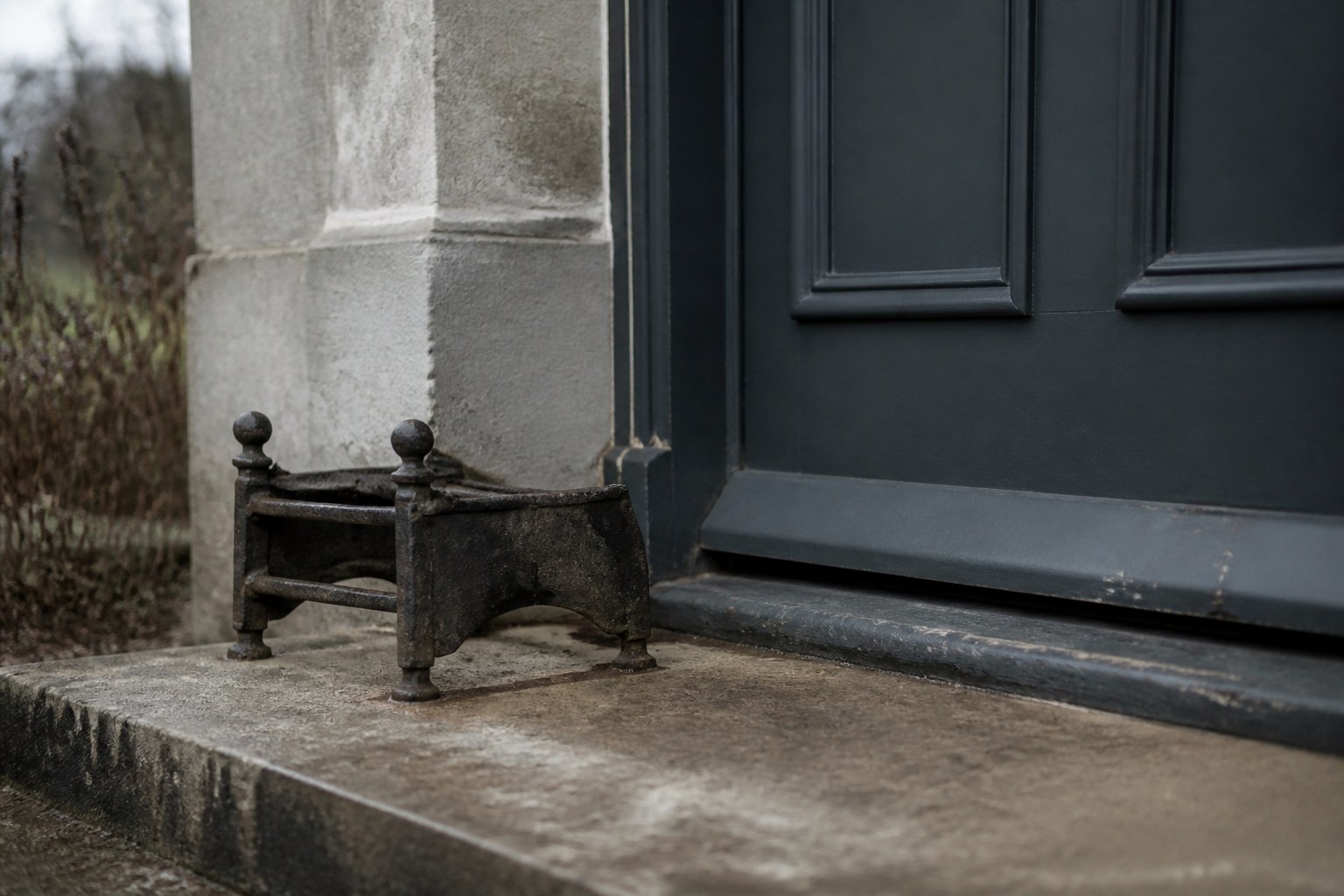 A stone doorstep with a worn cast iron boot scraper beside a closed dark panelled door