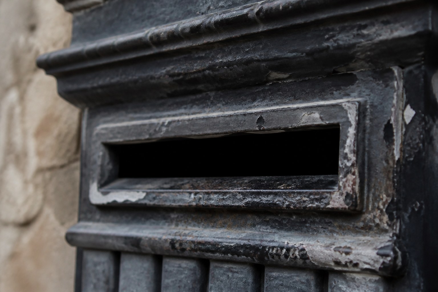The mouth of an old cast iron wall post box photographed close, the paint chipped around the slot