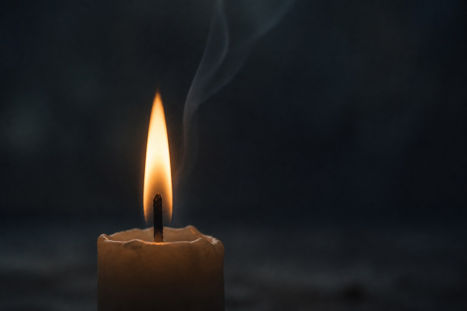 A single candle flame against a dark ground with the wick and a thin thread of smoke visible