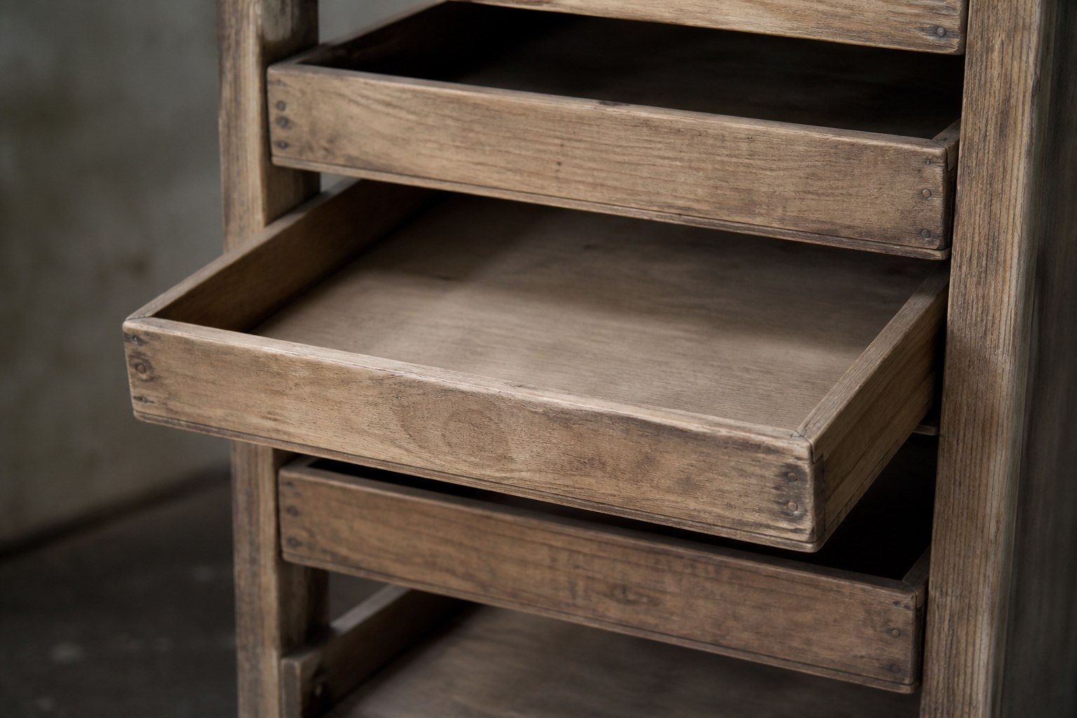 Three shallow empty wooden trays in a plain frame, the middle one pulled slightly out