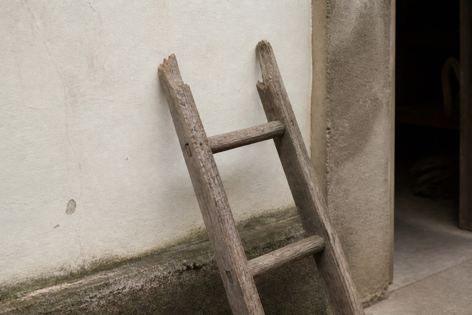 A wooden ladder against a wall with its top rungs broken away