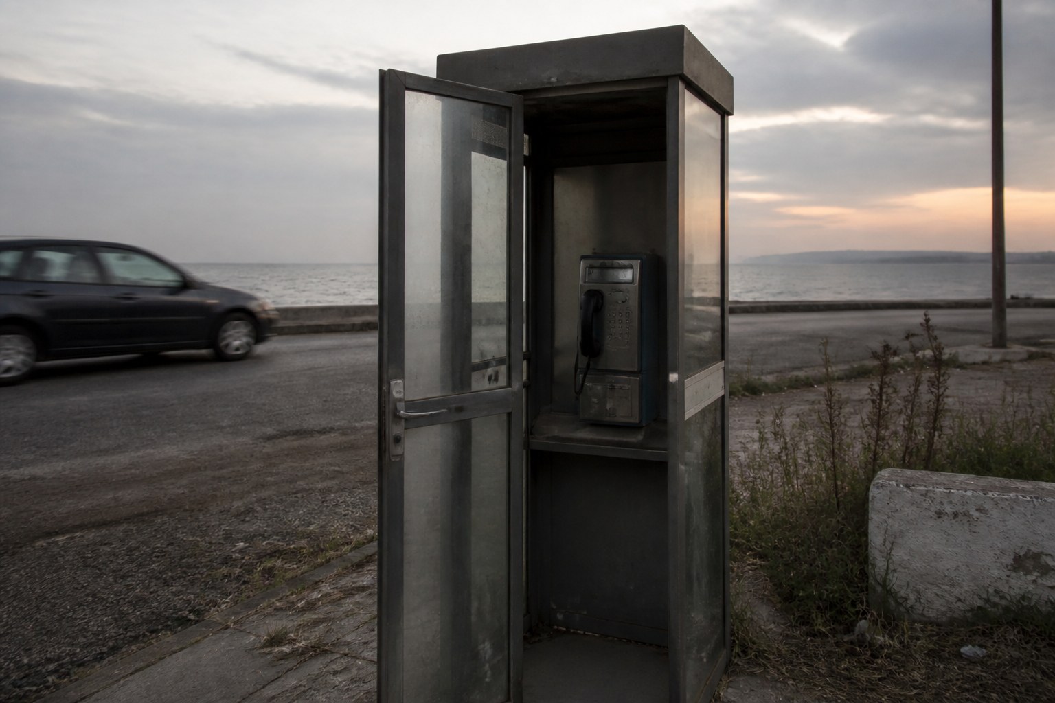 A public telephone box at a roadside at dusk with its door ajar