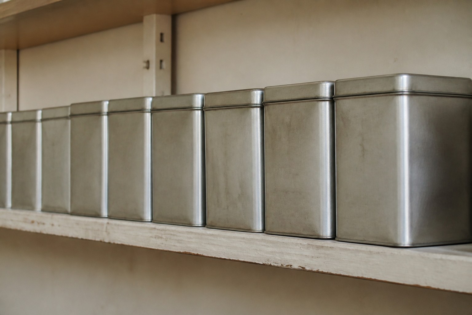 A row of identical unlabelled storage tins on a plain shelf
