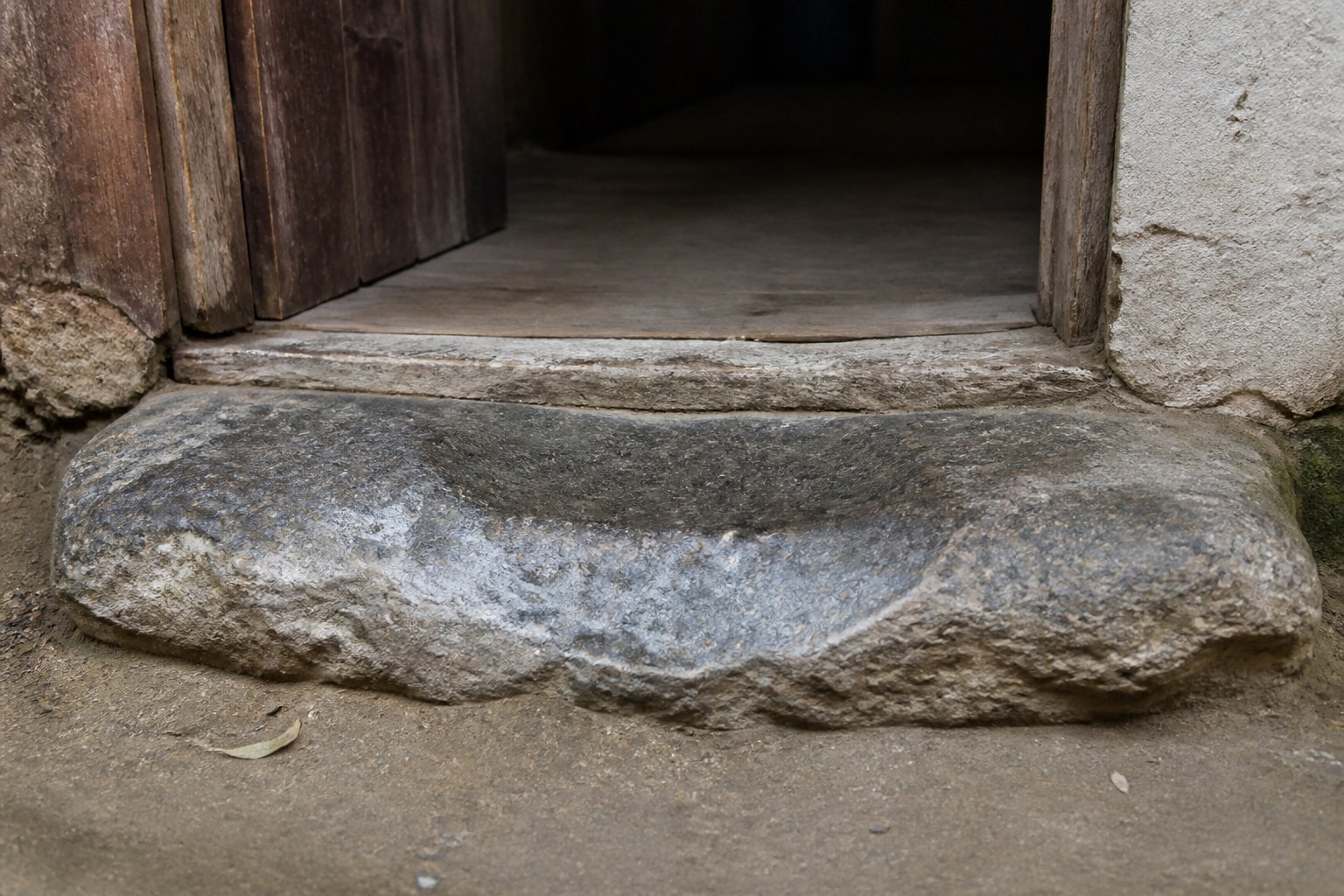 A worn stone threshold at a low doorway, the step hollowed by use