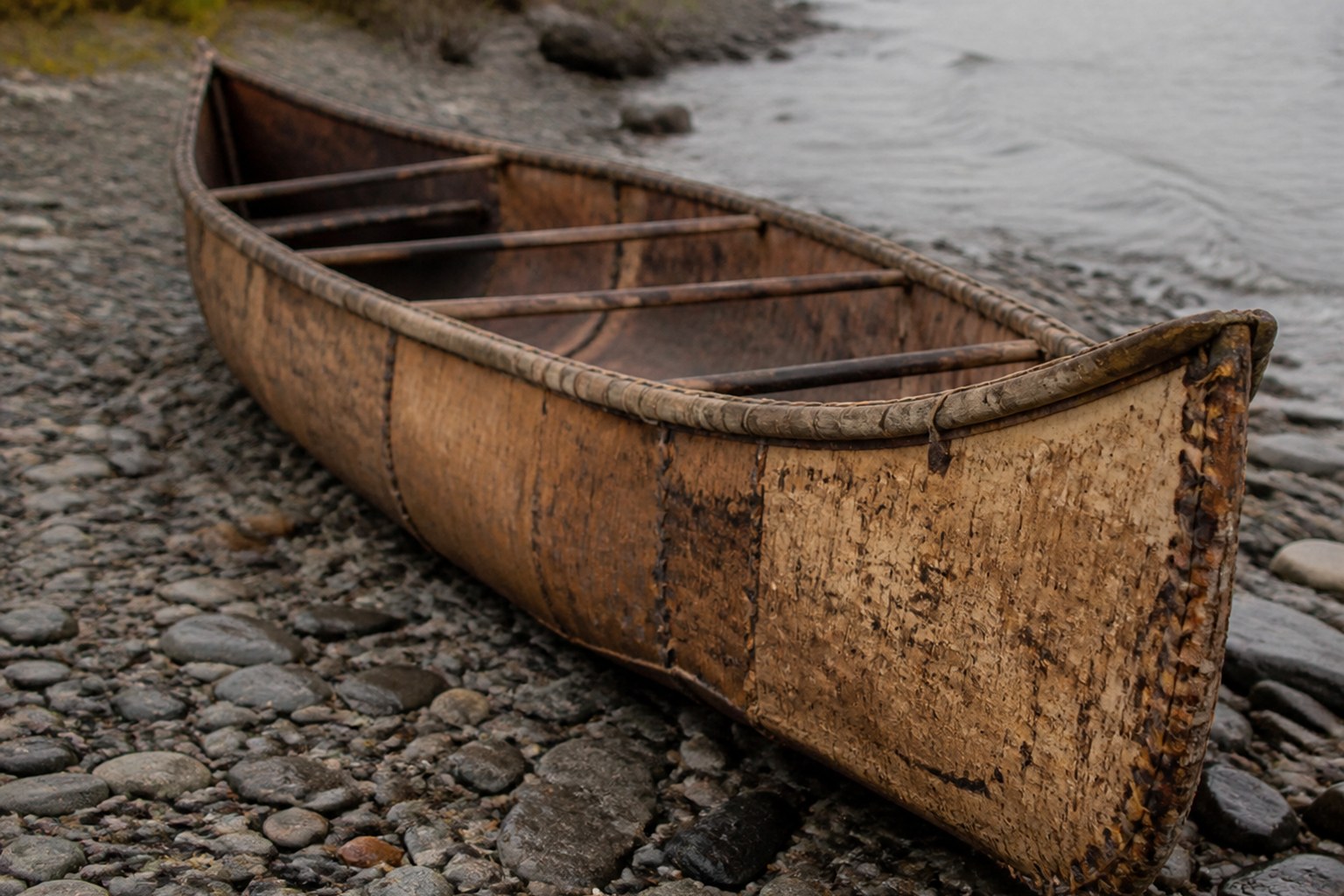 A birch bark canoe hull drawn up on a stony riverbank