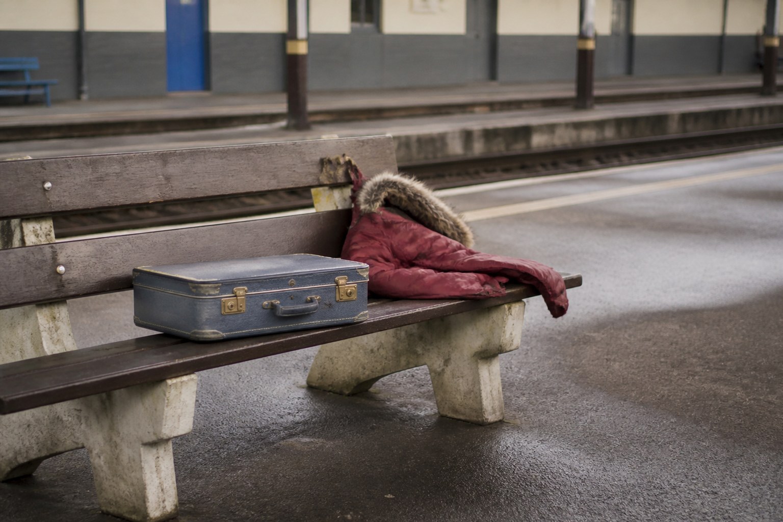 A small suitcase and a child's coat on a station bench