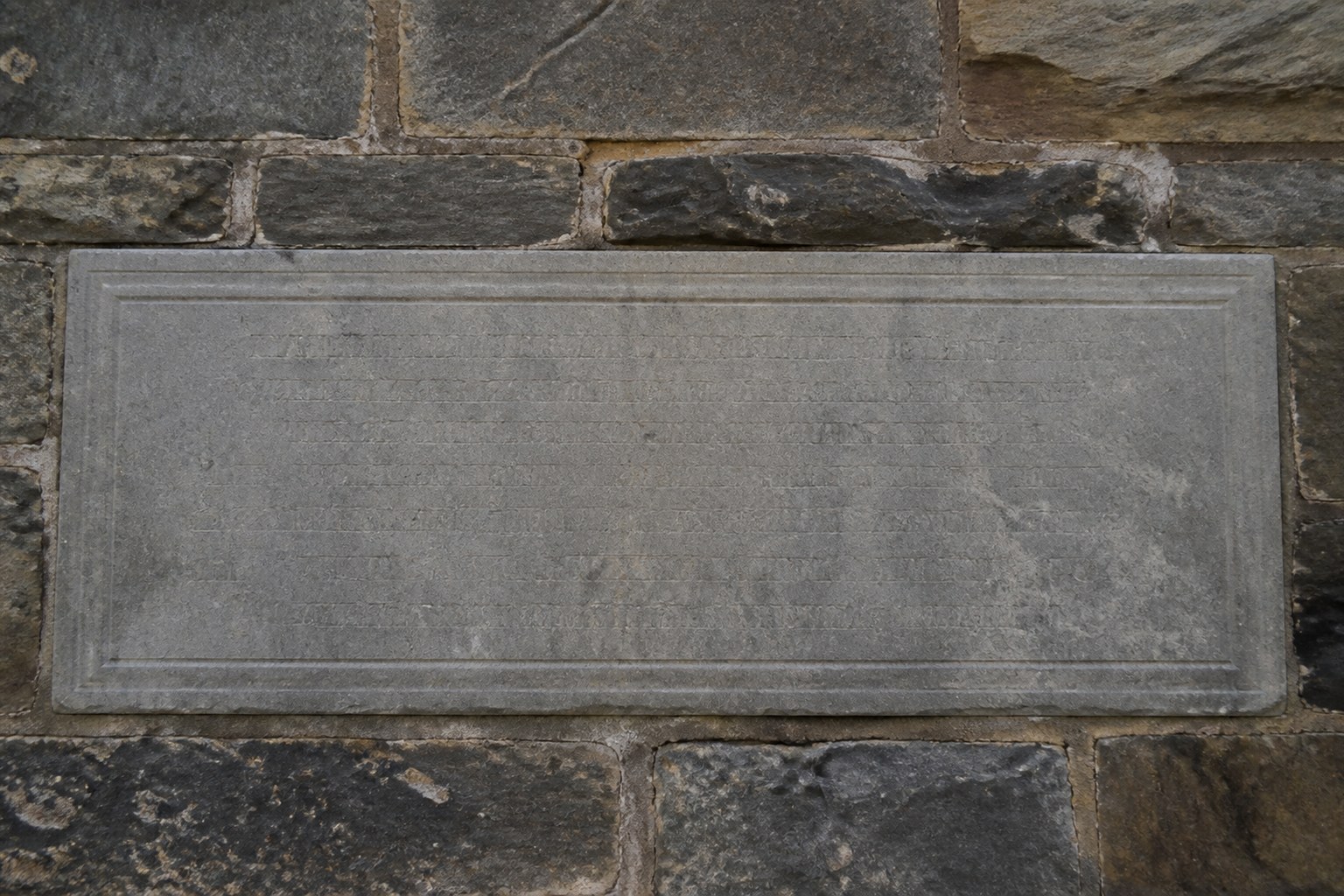 A stone donor plaque set into a wall with worn unreadable lettering