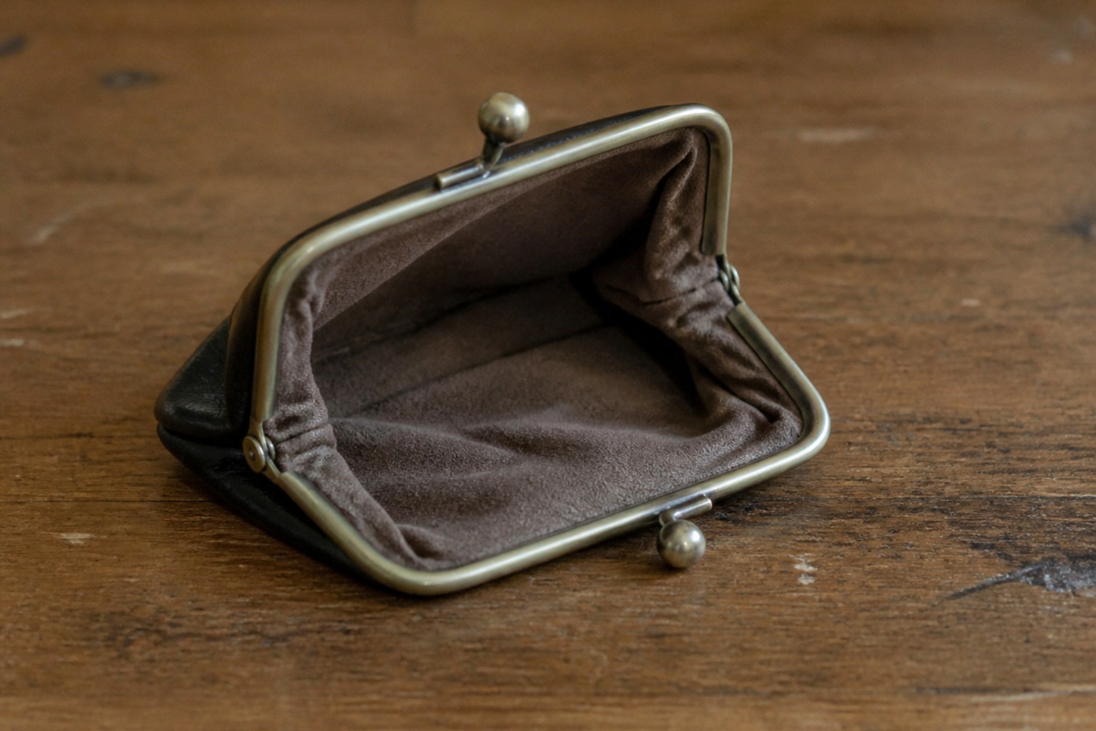 An open coin purse lying empty on a plain wooden table