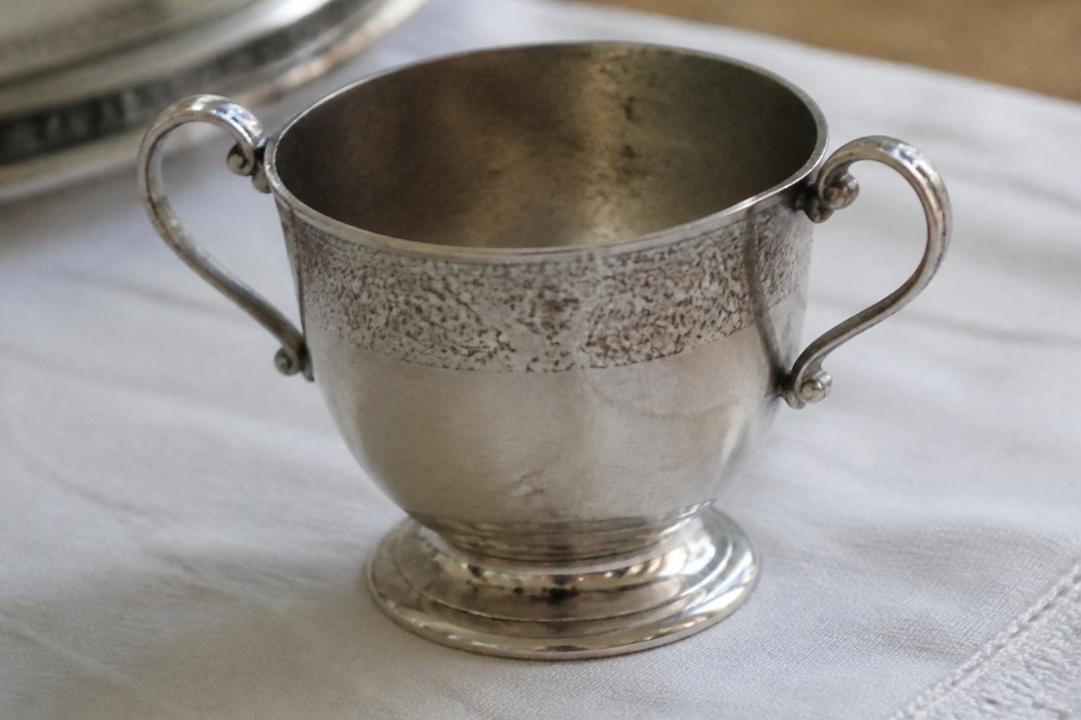 A small silver christening cup with worn engraving around the rim