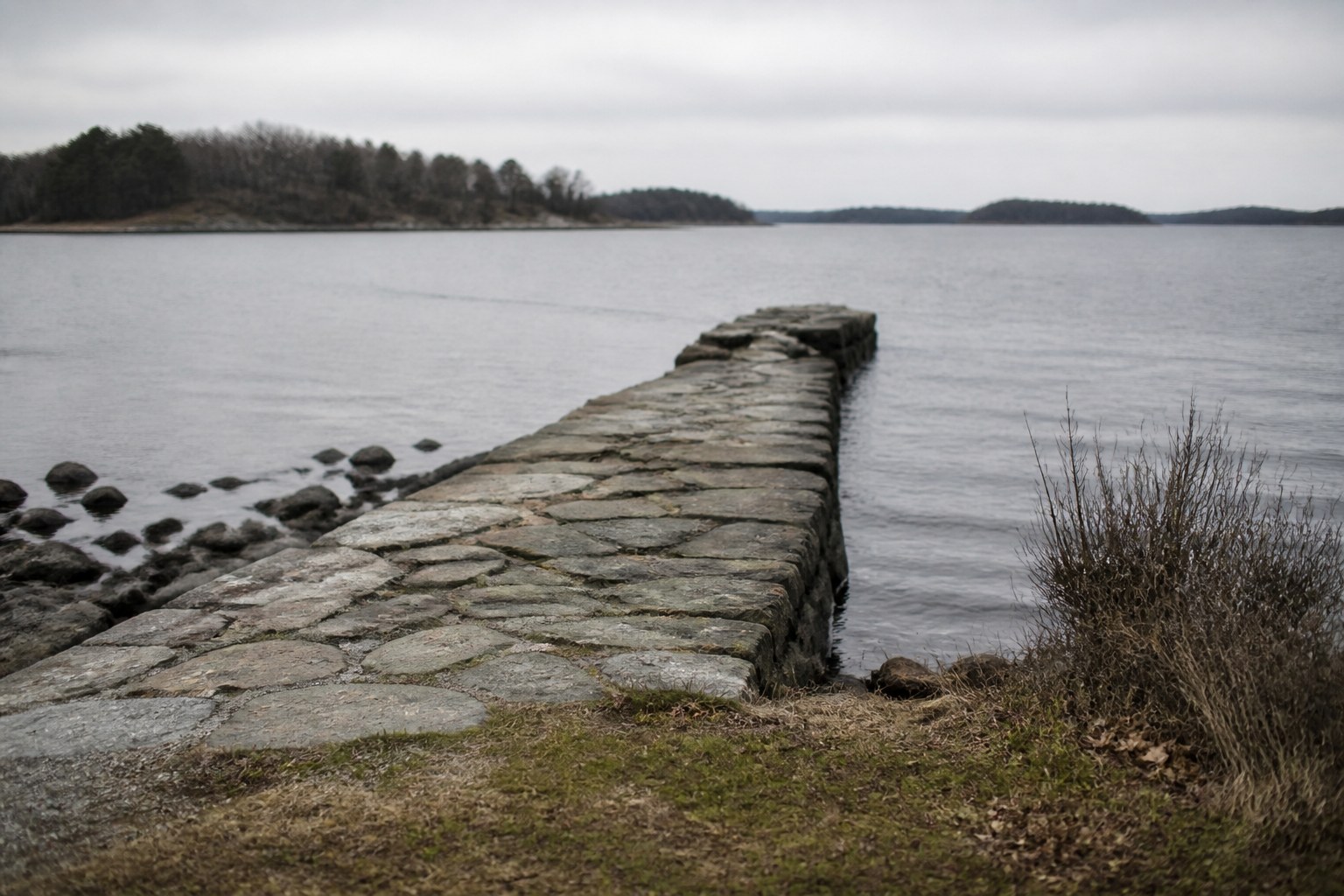 A short stone jetty running into grey water off a small island shore