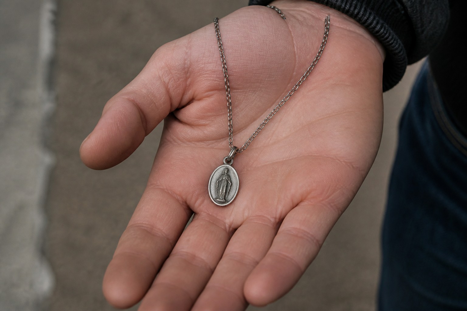 A small oval saint's medal on a thin chain lying in an open palm