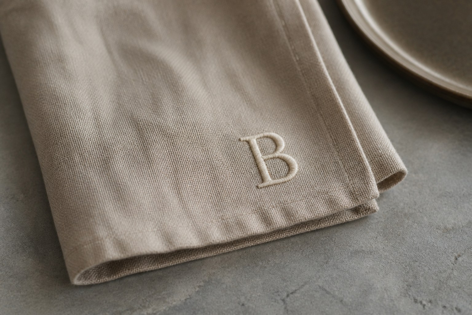 A capital letter B embroidered in cream thread on the corner of a folded linen napkin