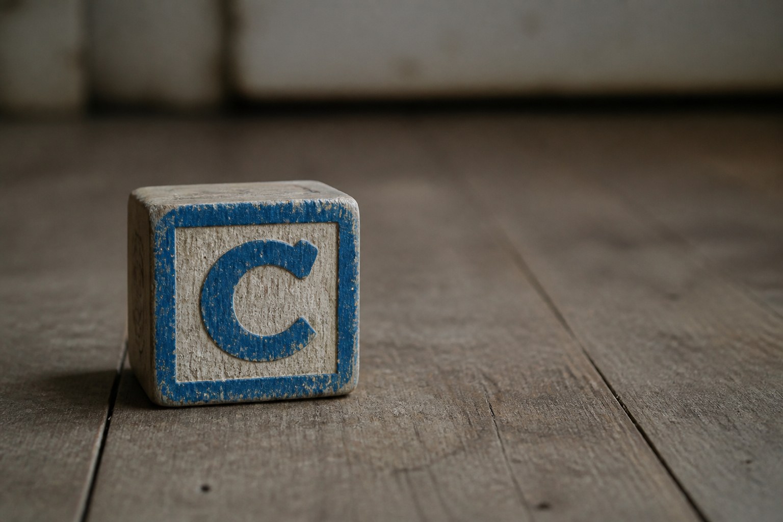 A worn painted wooden alphabet block showing the capital letter C, resting on bare floorboards