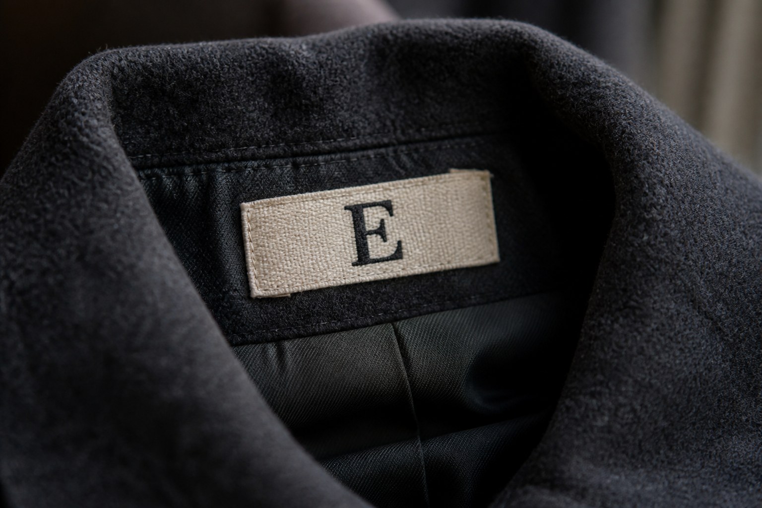 A woven cotton name tape carrying the capital letter E, stitched inside a coat collar