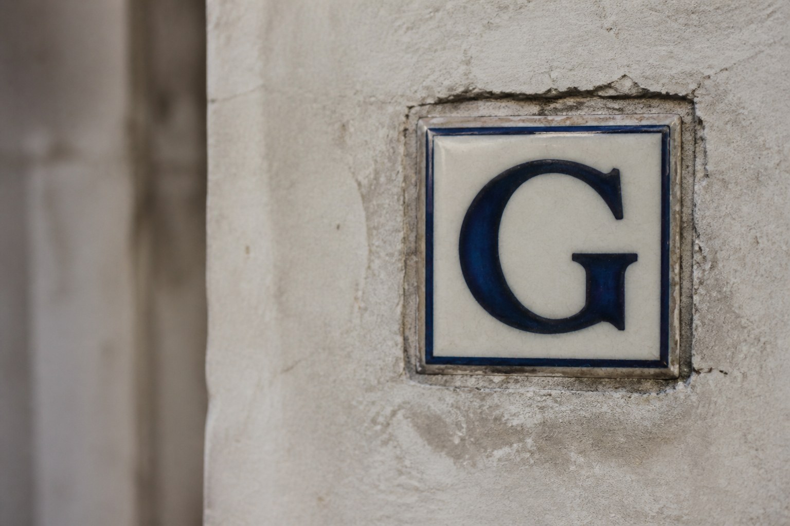 A single glazed ceramic wall tile bearing the capital letter G, set into plain plaster