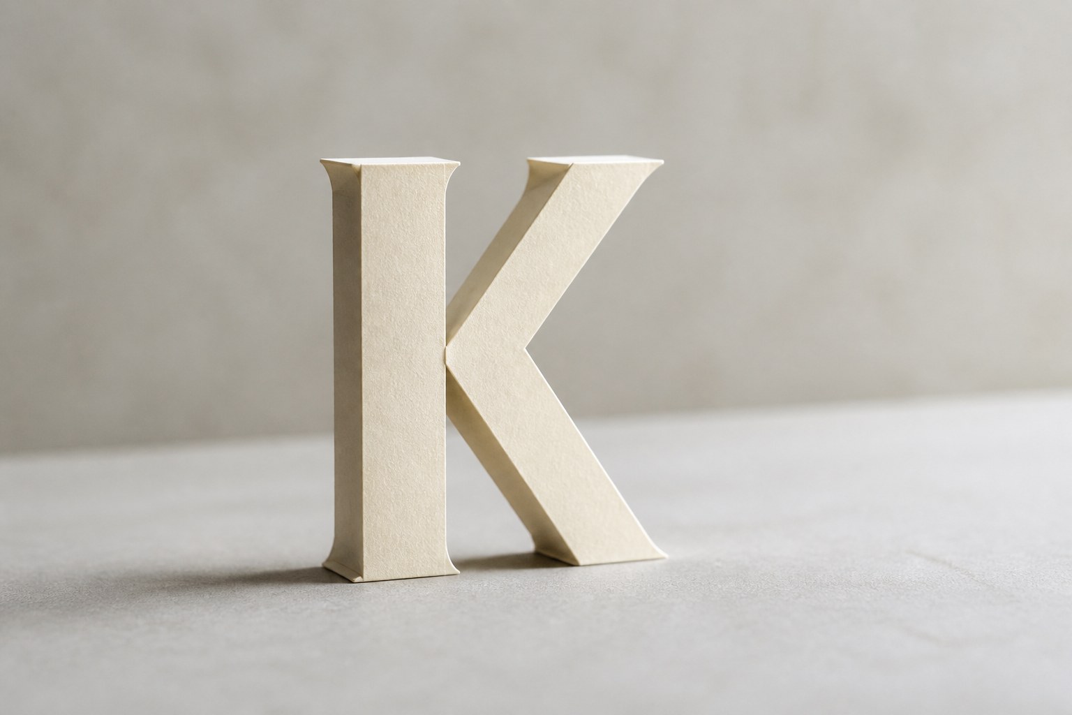 The capital letter K cut from folded cream paper, standing and casting a soft shadow