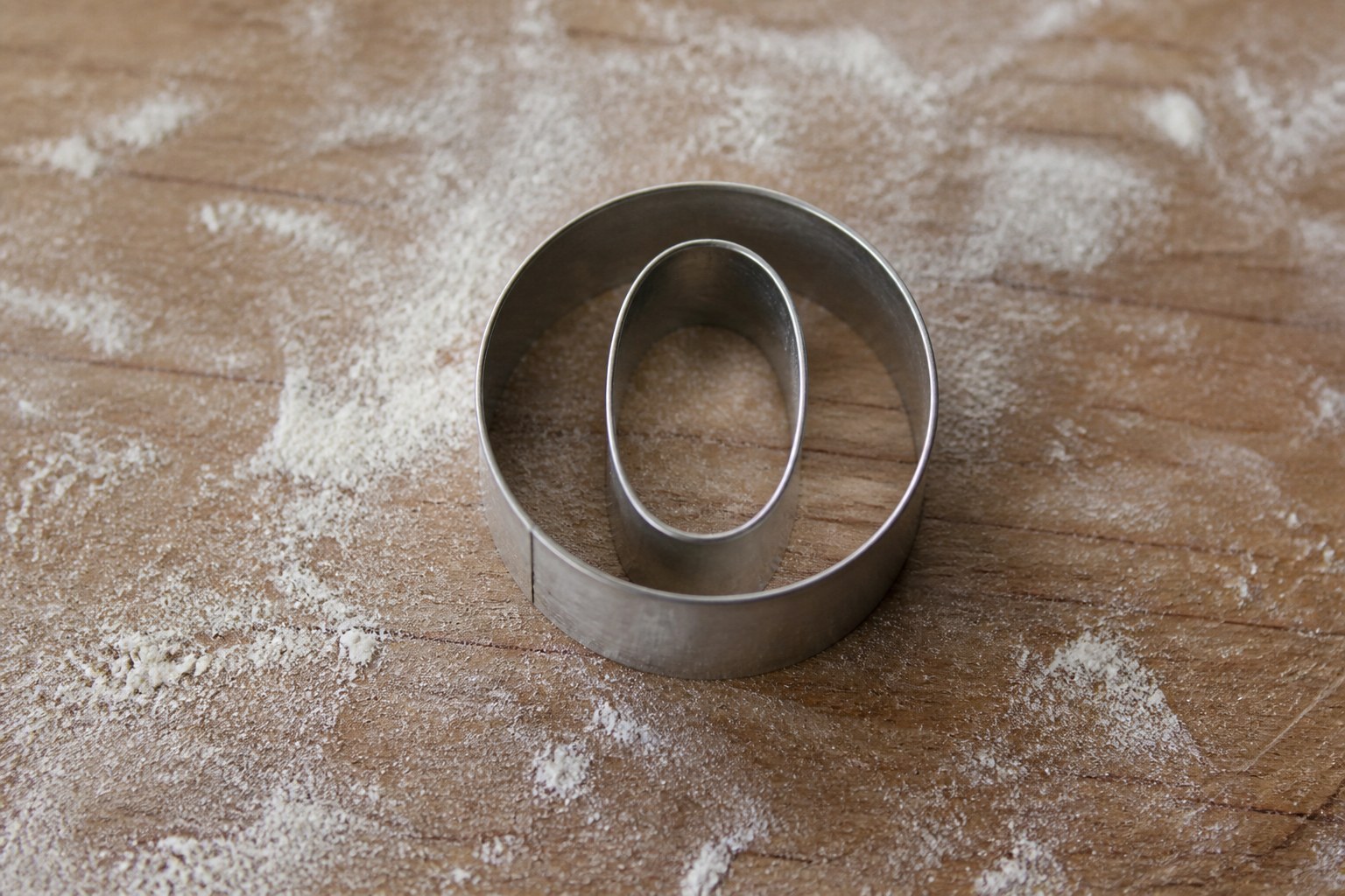 A metal biscuit cutter in the shape of the capital letter O resting on a floured wooden board